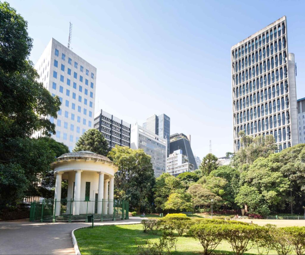 Paisagem que mostra uma pequena construção do parque, em contraste com os prédios que cercam o espaço.