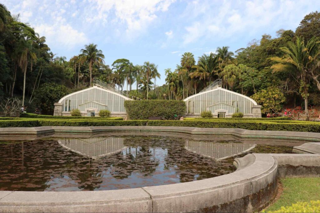 Paisagem que mostra as duas estufas do Jardim Botânico de São Paulo, refletidas na água de uma das fontes do parque.