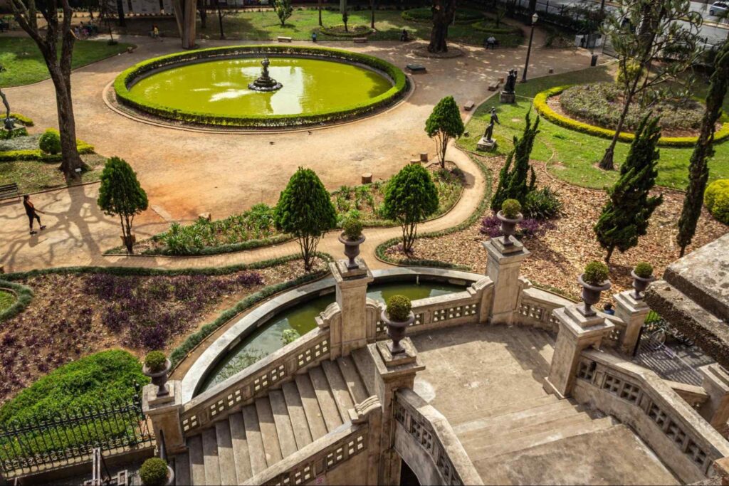 Uma das fontes de água do Parque Jardim da Luz, em frente às escadas em estilo colonial na Pinacoteca e ao jardim elaborado com pequenas árvores e caminhos de pedra.