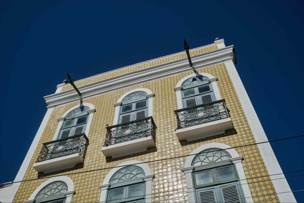 (Fachada de um casarão colonial em Aracati. É uma espécie de sobrado revestido com azulejos amarelos e com fileiras horizontais de janelas azuis.)