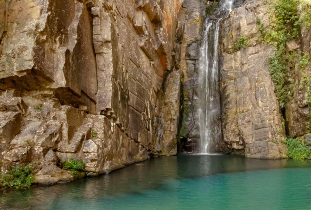 Incrível foto da Cachoeira Véu da Noiva em Serra do Cipó, com poço azul em contraste com paredão de rocha amarelada.