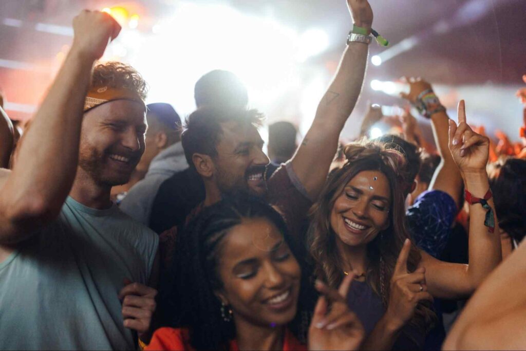 Foto de um grupo de 4 amigos sorrindo e dançando ao som ao vivo em festival.