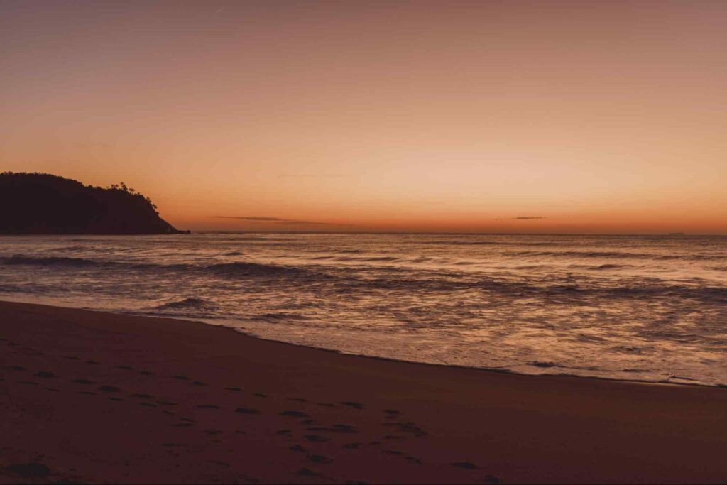 Pôr do sol na Praia de Itapema SC. Mar sem ondas e parte da faixa de areia iluminados pelo entardecer.